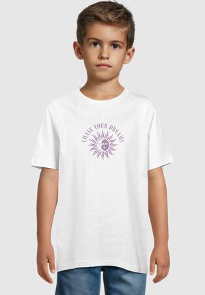 Vit bomull t-shirt med en lila soldesign och texten "FÖJ DIN DRÖM" ovanför. Korta ärmar och avslappnad passform.