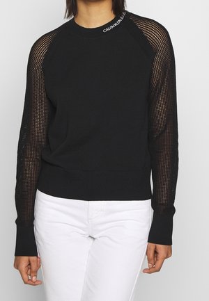 Suéter negro con mangas de malla, puños acanalados y cuello con el logo "CALVIN KLEIN JEANS". Tela principal lisa y acentos texturizados.