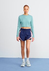 Svetlo modrý dlhý rukáv crop top v kombinácii s námorníckymi šortkami s ružovými bočnými panelmi. Model má na sebe biele ponožky a svetlošedé športové topánky.