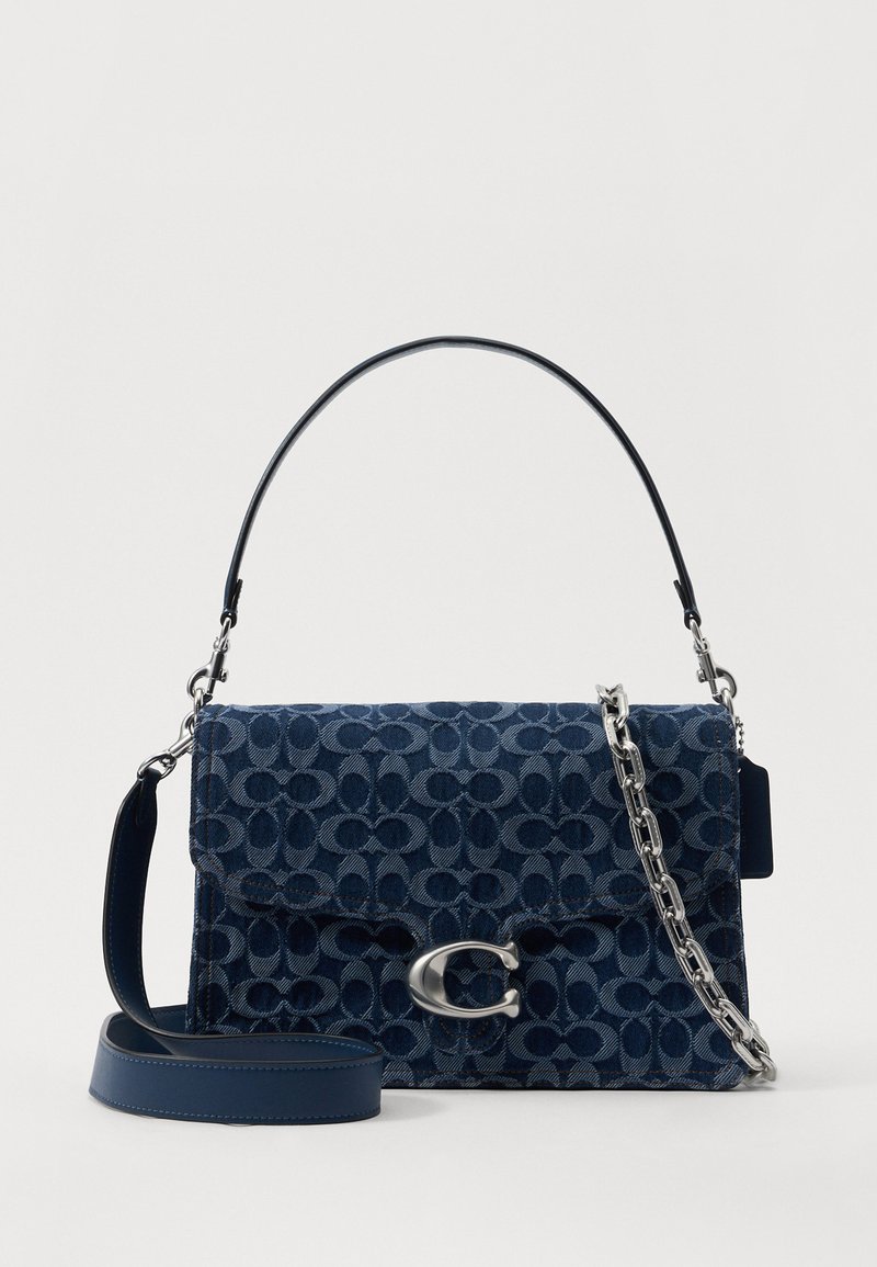 Navy blue denim handbag with a geometric pattern, silver hardware, detachable chain, and leather strap; flap top closure.
