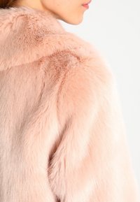 Ljusrosa fuskpälsjacka med en mjuk, texturerad yta, med hög krage och något oversize passform vid axlarna.