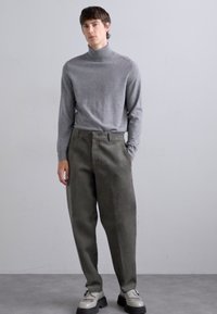 Maglione grigio a collo alto, pantaloni larghi verde oliva e scarpe grigie con suole nere. Design semplice e minimal con tessuto testurizzato.