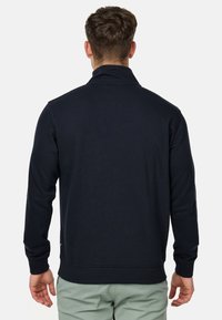Chaqueta de pullover navy con cuello alto, fabricada con una mezcla de algodón. Presenta puños y dobladillo acanalados, textura suave con detalles de costura mínimos.
