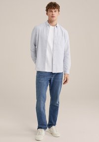 Lichtblauw gestreept overhemd met knopen over een wit T-shirt, gecombineerd met blauwe jeans en witte sneakers. Het overhemd heeft een borstzakje.