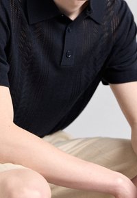 Námořnická pletená polo košile s texturovaným vzorem, límečkem a dvouknoflíkovým zapínáním. Krátké rukávy a měkká tkanina.