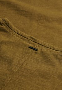 Olive zielony bawełniany materiał o gładkiej fakturze, z widoczną linią szwu i małym czarnym detalem z napisem "Superdry".