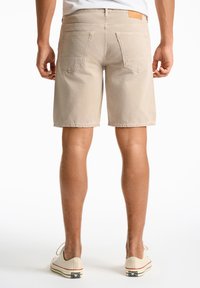 Beige spijkerbroek shorts met een rechte pasvorm, voorzien van twee achterzakken en een leren label op de taille, gecombineerd met canvas sneakers.