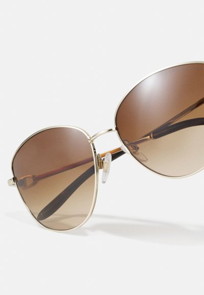 Brown gradient sunglasses with a gold metal frame, oversized lenses, and black temple arms. Clear nose pads and sleek, modern design.