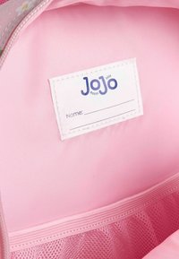 Roza tkanina notranjosti torbe, ki vsebuje belo oznako z napisom "JoJo" in prostorom za ime. Vključuje mrežasto žep na dnu.