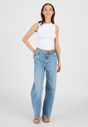 Valkoinen hihaton toppi yhdistettynä vaaleansinisiin leveälahkeisiin farkkuihin ja kuvioituun harmaaseen vyöhön. Mallilla on päällään hiekansävyiset korkeat kengät. Yksinkertainen tausta.