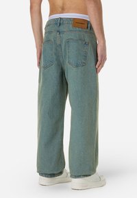 Light blue loose-fitting jeans with a high waist, five-pocket design, and a brown leather brand tag at the back. Smooth denim texture.