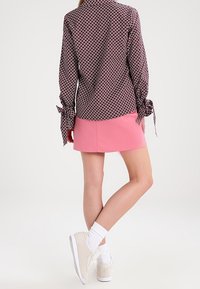 Långärmad, mönstrad skjorta med slipsar vid muddarna, tillsammans med en rosa minikjol och vita sneakers. Slät tyg, figurnära design.