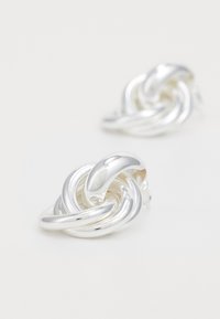 Boucles d'oreilles en argent en forme de nœud, présentant une texture lisse et brillante ainsi qu'un design entrelacé. Elles sont équipées d'un fermoir à tige pour un port en toute sécurité.