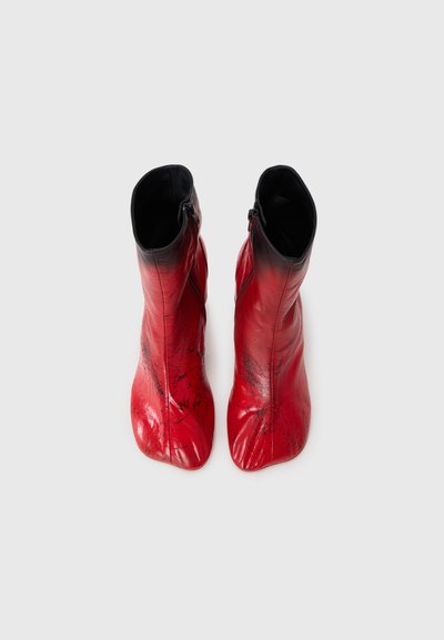 Röda läderankelboots med en blank yta, dragkedjestängning och spetsig tådesign, med svarta accenter och en strukturera yta.
