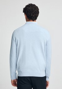 Jasnoniebieski sweter z dzianiny z długimi rękawami, ściągaczami przy mankietach i u dołu oraz kołnierzykiem. Gładka tekstura, klasyczny fason, minimalne detale.