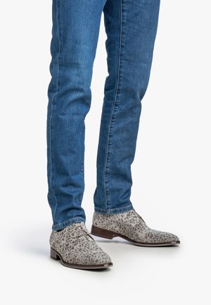 Zapatos gris con estampado de leopardo, hechos de suave ante, con punta redonda, diseño de cordones y tacón de madera de altura media, combinados con jeans azules.