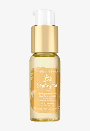 L'huile de coiffage Bumble and bumble Bb. dans une petite bouteille en verre transparente avec un capuchon doré. Liquide jaune à l'intérieur, étiqueté avec un texte blanc.