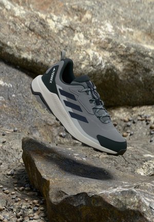 Graue Sportschuhe mit dunkelgrünen Akzenten, Obermaterial aus Mesh und weißer Sohle, mit drei schwarzen Streifen und verstärkter Ferse.