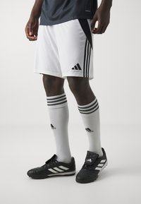 Hvite idrettsshorts med svarte sidepaneler, kombinert med svarte fotballsko og knelange hvite sokker med tre svarte striper og logoer.