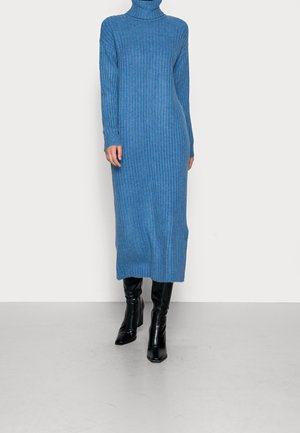 Robe col roulé en tricot bleu avec texture côtelée, manches longues et silhouette droite, associée à des bottes noires montant jusqu'aux genoux.