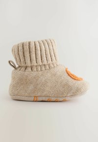 Neulepuku vaaleassa beige-värissä ribbaamalla, oranssilla yksityiskohdalla ja liukumattomalla pohjalla. Rakenteellinen päällinen pehmeällä kankaan pinnalla.