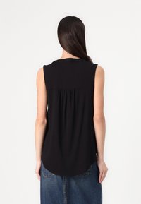 Ärmelloses schwarzes Top mit rundem Halsausschnitt, gefaltetem Rückendetail und einem längeren, geschwungenen Saum, aus glattem, leichtem Stoff.