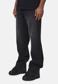 Czarne dżinsy o luźnym kroju, z wyblakłą teksturą, subtelnymi przednimi kieszeniami, połączone z czarnymi butami sportowymi.