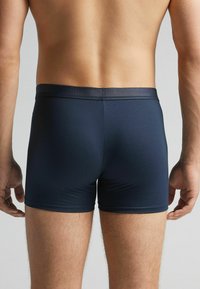 Tyrkysové boxerky vyrobené z hladké tkaniny s elastickým pasem, se přiléhavým střihem a minimálními švy.