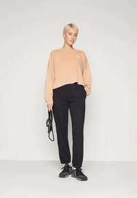 Ohlapna, svetlo breskev obleka s dolgimi rokavi in logotipom, v kombinaciji s črnimi ožjimi trenirkami in črnimi športnimi čevlji. Preprost in sproščen dizajn.