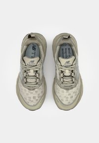 Chaussures de sport gris clair avec tige en maille, semelles texturées et coques de protection renforcées. Lacets et logo dans un beige doux et un bleu contrastants.