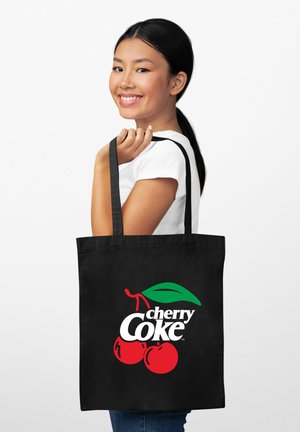 Czarna torba typu tote z kolorowym logo "cherry Coke", w którym znajdują się czerwone wiśnie i zielony liść. Torba ma długie, mocne uchwyty.