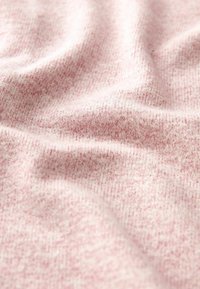 Weicher, rosa gestrickter Stoff mit sichtbarer Textur und leichten Falten, die sanfte Schatten und Tiefe erzeugen.