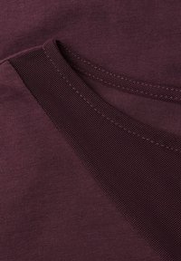 Tessuto bordeaux con una superficie liscia e un dettaglio in rete a contrasto sul colletto, che mette in risalto una fusione di texture.