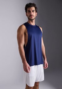 Marinblå ärmlös atletisk linne i slätt, lätt material, kombinerad med vita shorts. Enkel, figurnära design med minimal detaljering.