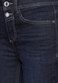 Mörkblå denimjeans med en slät textur, ljus sömnad och silverdetaljer, med en framficka och en klassisk design med fem fickor.
