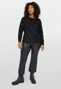 Maglione nero a maglia con maniche lunghe, caratterizzato da file diagonali di piccole borchie argentate. Abbinato a pantaloni in pelle nera aderenti e stivaletti.