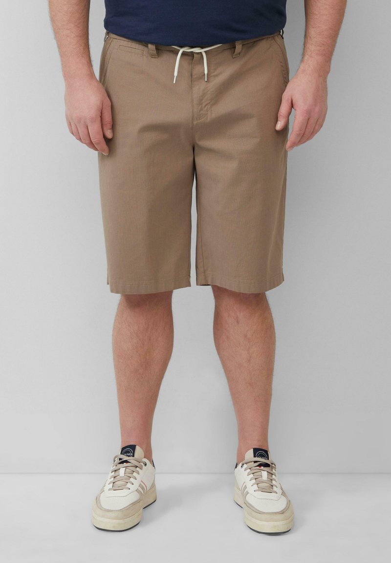 Braune Baumwoll-Shorts mit geradem Bein, ausgestattet mit einem Gummizugbund und Seitentaschen, kombiniert mit cremefarbenen Sneakers.