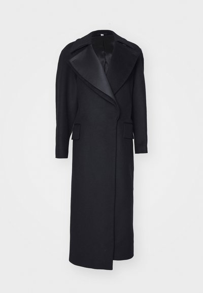 Cămașă lungă din lână, de culoare neagră, cu un guler ascuțit și buzunare în față. Design personalizat cu o siluetă elegantă și detalii minime.