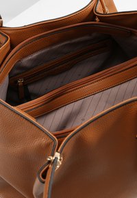 Braune Lederhandtasche mit strukturiertem Finish. Das Innere verfügt über ein braun gestreiftes Futter und mehrere mit Reißverschluss gesicherte Fächer zur Organisation.