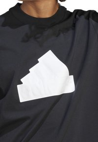 Czarna bawełniana koszulka z wyraźnym białym gumowanym logo Adidas, z okrągłym dekoltem i krótkimi rękawami. Gładka tekstura.