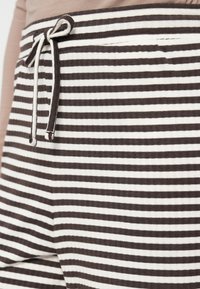 Brown and white striped fabric with a soft texture, featuring an adjustable drawstring at the waist and a side pocket detail.