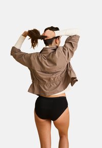 Brun cropped jakke med elastisk talje, over en hvid langærmet top og sorte højtaljede nederdele. Jakken har en afslappet pasform og minimal detaljer.