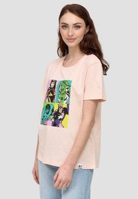 Vaaleanpunainen t-paita, joka on valmistettu pehmeästä puuvillasta. Edessä on värikäs sarjakuvamainen grafiikka supersankareista. Lyhyet hihat, rento malli.