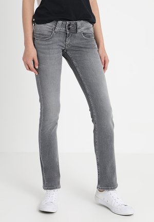 Person wearing slim-fit faded gray jeans, black top, and white sneakers, standing against a plain white background.