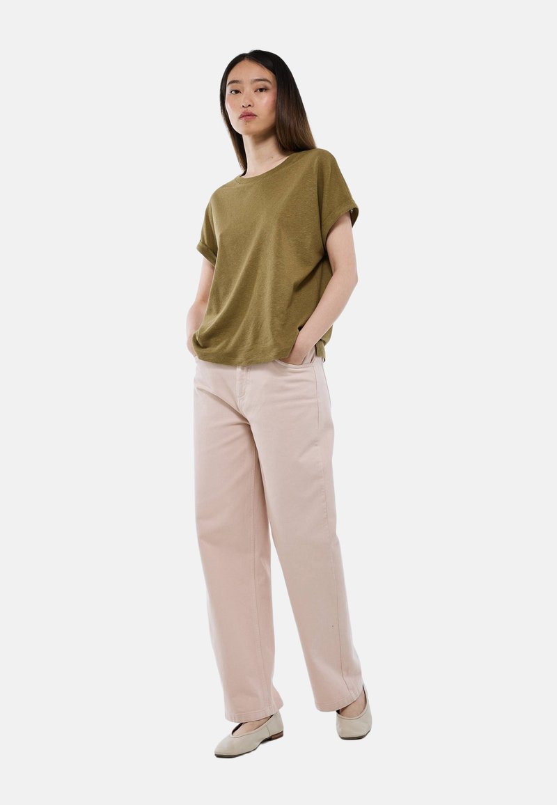 T-shirt court vert olive à manches courtes, coupe décontractée, associé à un pantalon large rose clair. Le modèle se tient les mains dans les poches, portant des chaussures plates beiges.