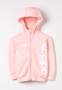 Rosa zip-up hoodie i mjukt tyg med huva, ribbade handlingar och en vit adidas-logotyp som är tryckt vertikalt på framsidan.