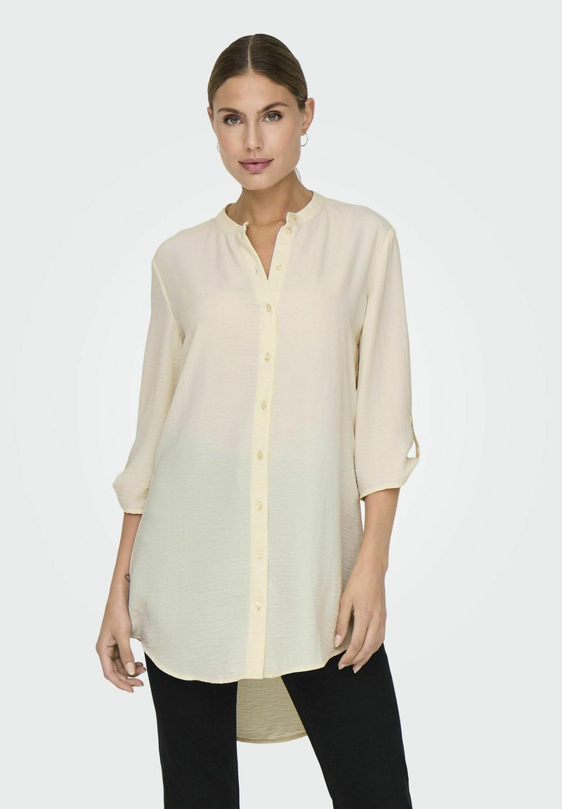 Light cream button-up shirt with a mandarin collar, long sleeves rolled to elbow, and a straight hem. Smooth, lightweight fabric.