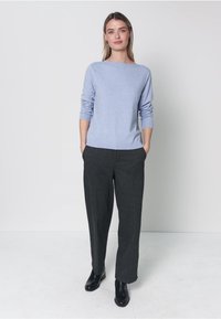 Pull bleu clair à manches longues, associé à un pantalon large gris foncé et des bottines noires. Textures simples et lisses avec une coupe décontractée.