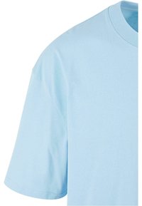 Tricou din bumbac de culoare albastru deschis, cu guler rotund, mâneci scurte și o textură netedă, simplă. Prezintă cusături standard pe margini.