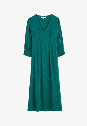 Robe teal avec un décolleté en V, des manches bouffantes 3/4 et des poignets smockés. Présente des motifs de pois blancs sur l'ensemble du tissu, avec une silhouette fluide.
